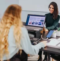 Two women working and smiling in front of computers